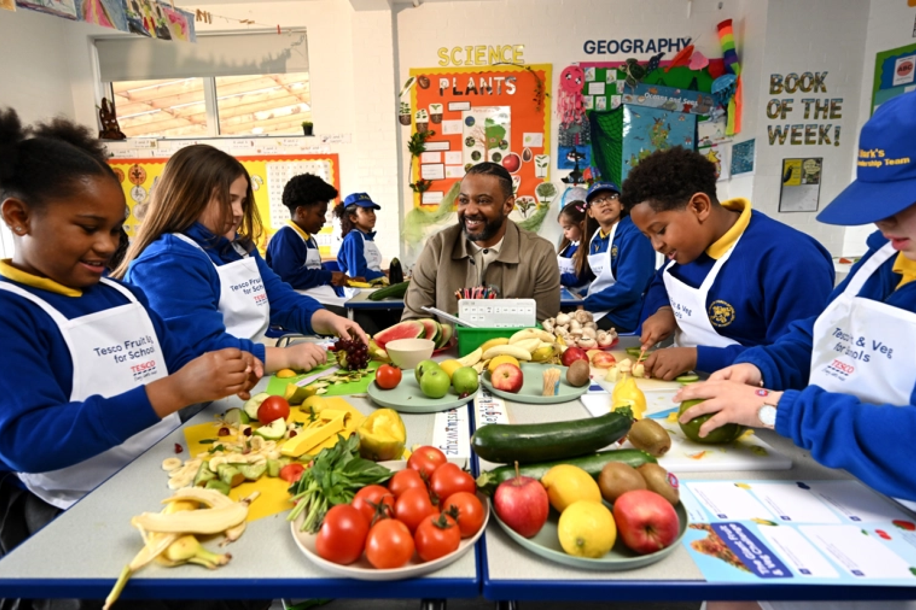 Britische Schulkinder sitzen gemeinsam an einem Tisch und schneiden Obst und Gemüse.