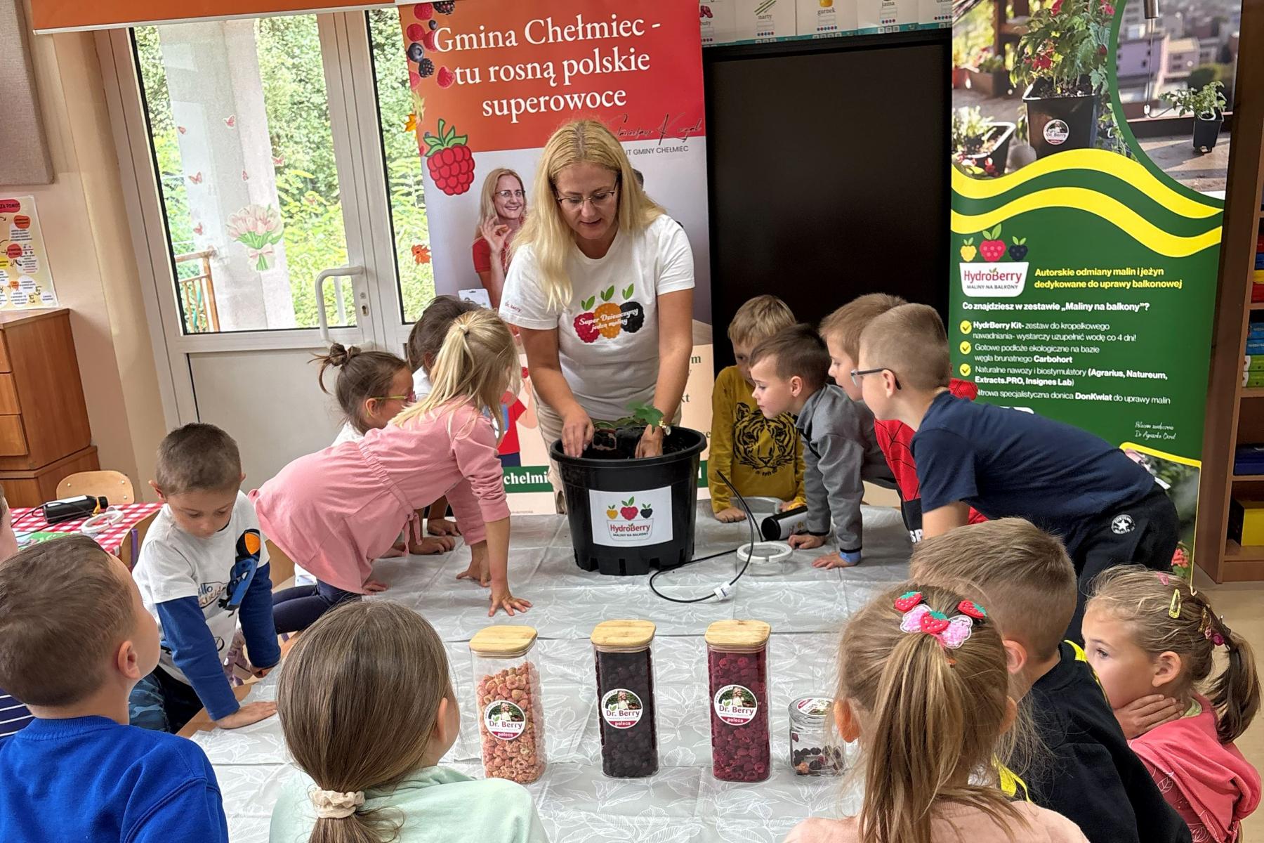 Frau pflanzt Beerenpflanze in Topf während Kinder um den Tisch stehen und zugucken