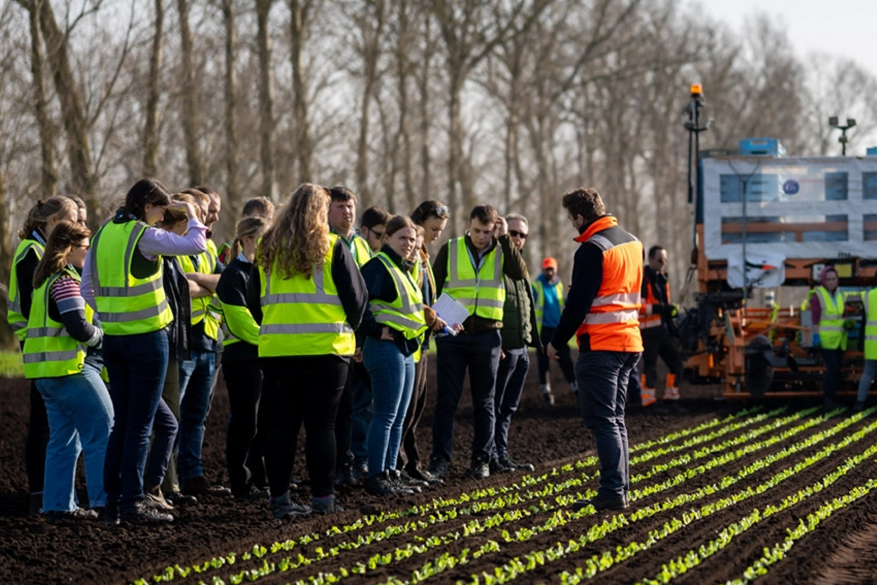 Junge britische Landwirte stehen in hellen Sicherheitswesten vor einem Feld.