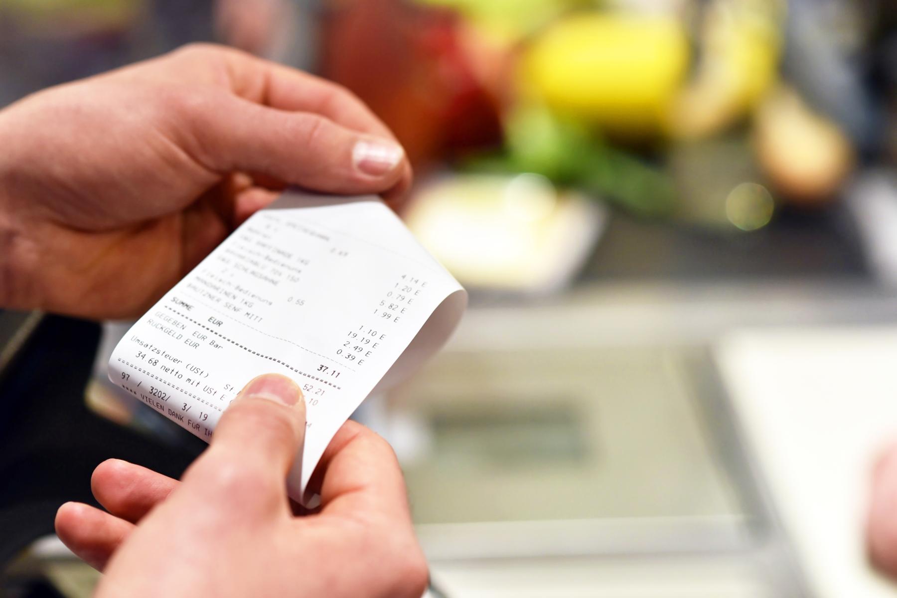 Eine Person hält einen ausgedruckten Kassenbon an einer Supermarktkasse in den Händen.