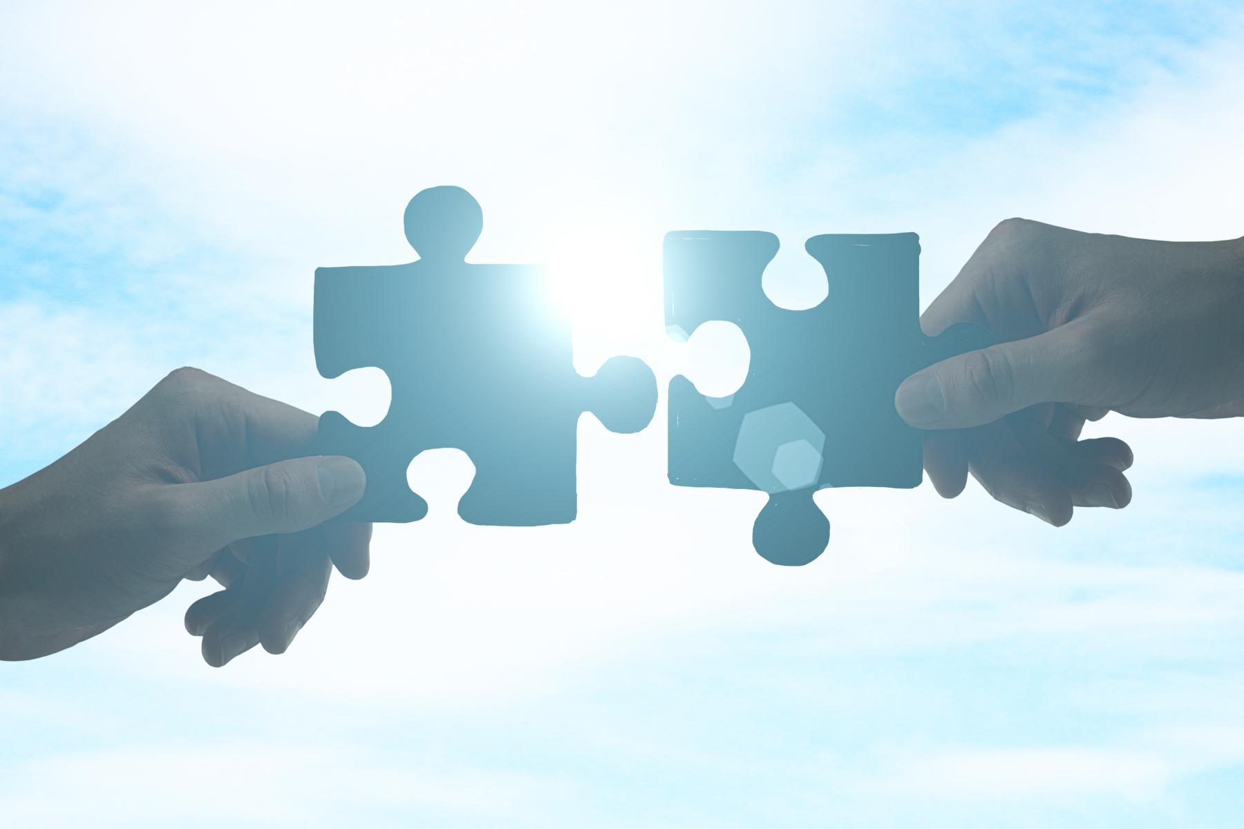 zwei Hände stecken zwei Puzzleteile zusammen