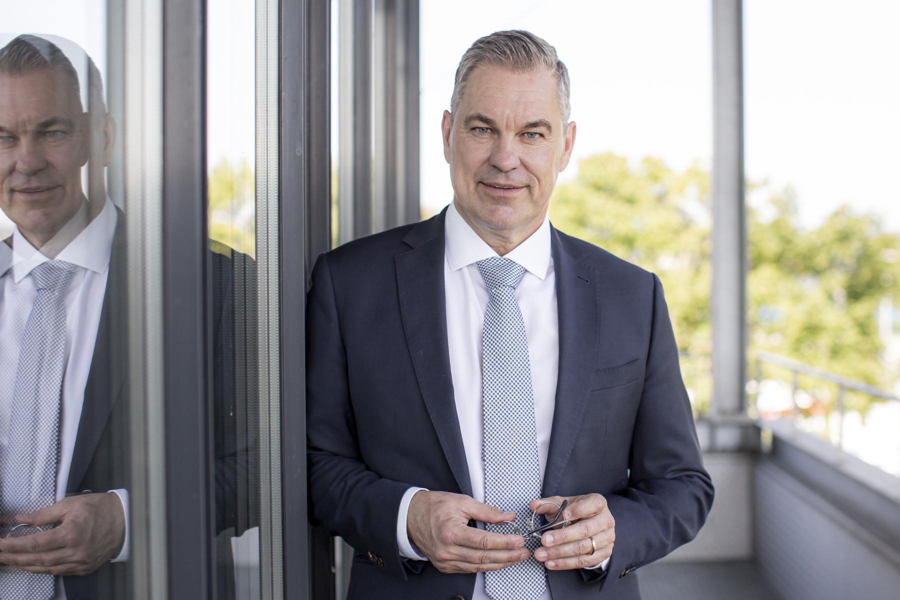 Ein Mann mit weißem Hemd und hellblauer Krawatte und dunkelblauer Jacke. 