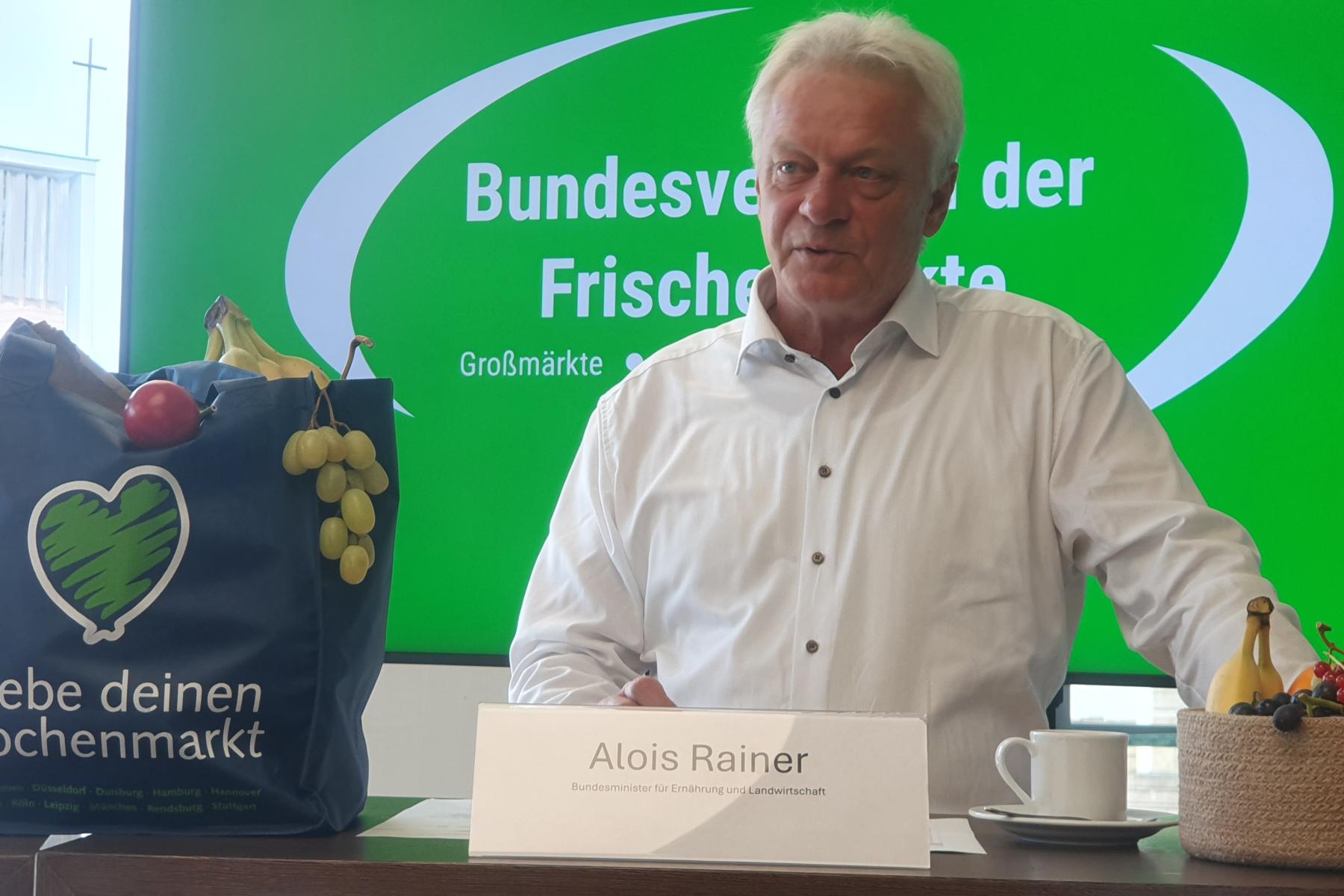 Mann steht an Tisch mit Tasche neben sich, die mit Obst und Gemüse gefüllt is