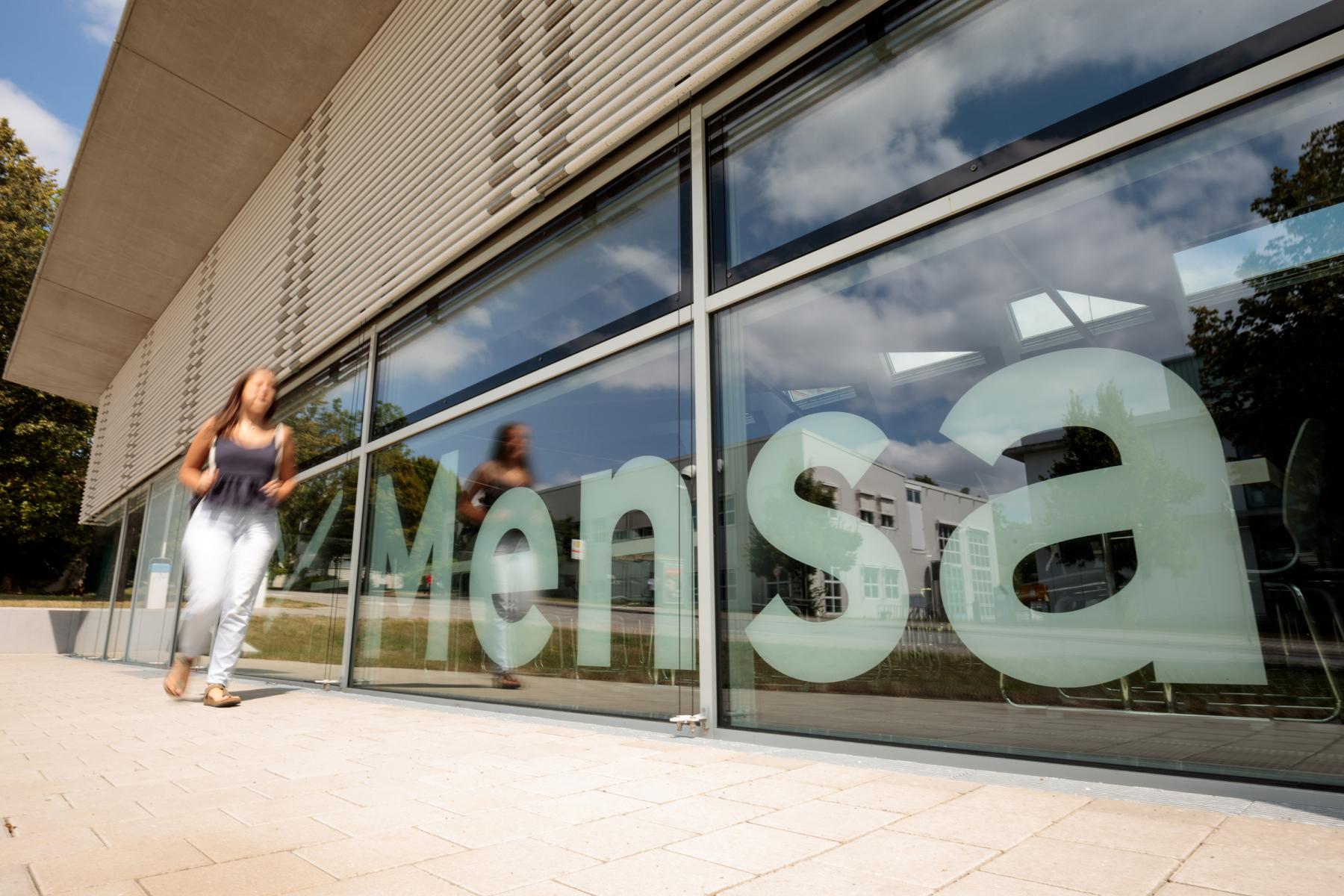 Person läuft vor Gebäude mit Mensa-Schriftzug vorbei