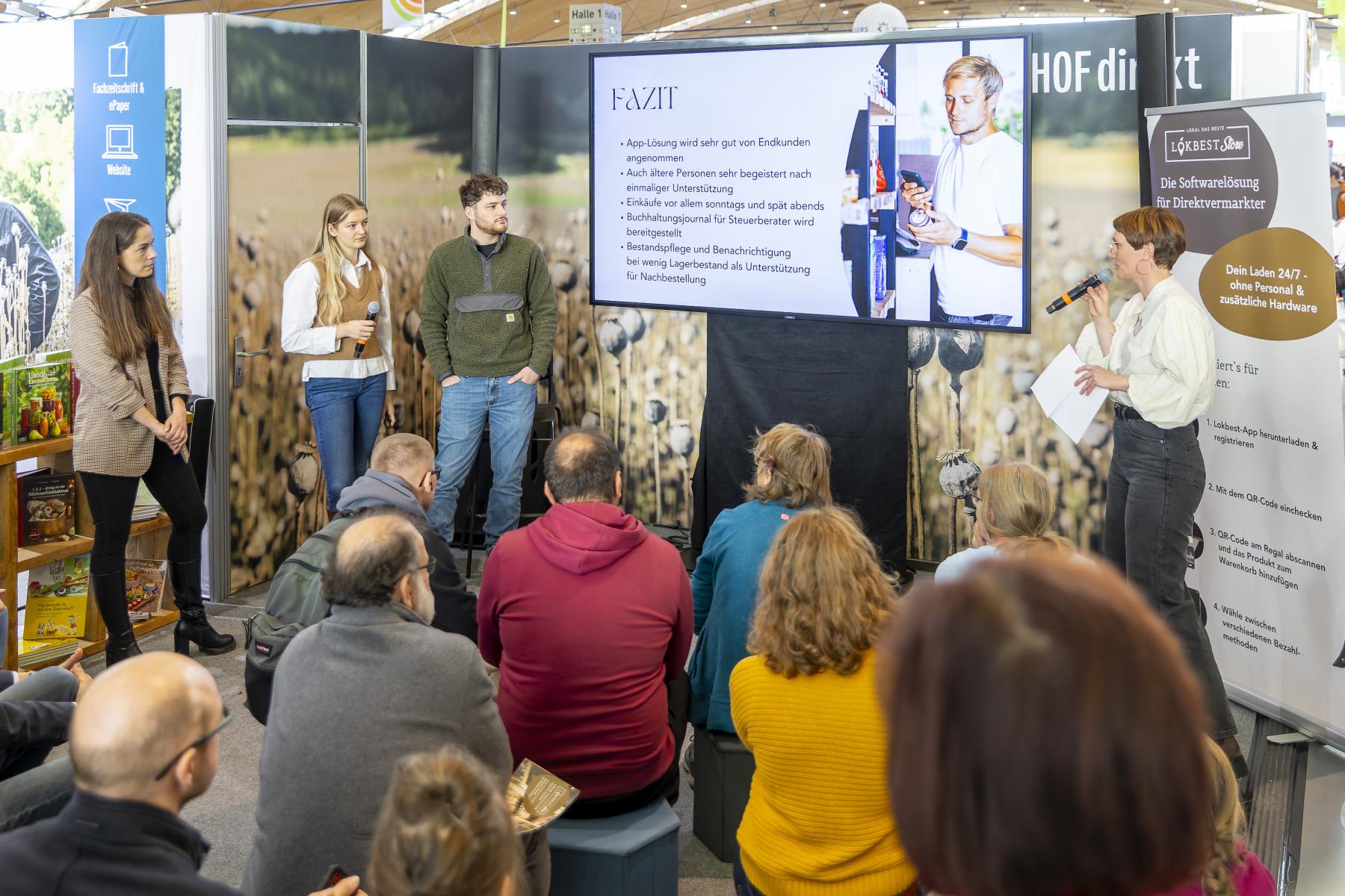 Referenten stehen neben Infoscreen vor Plenum