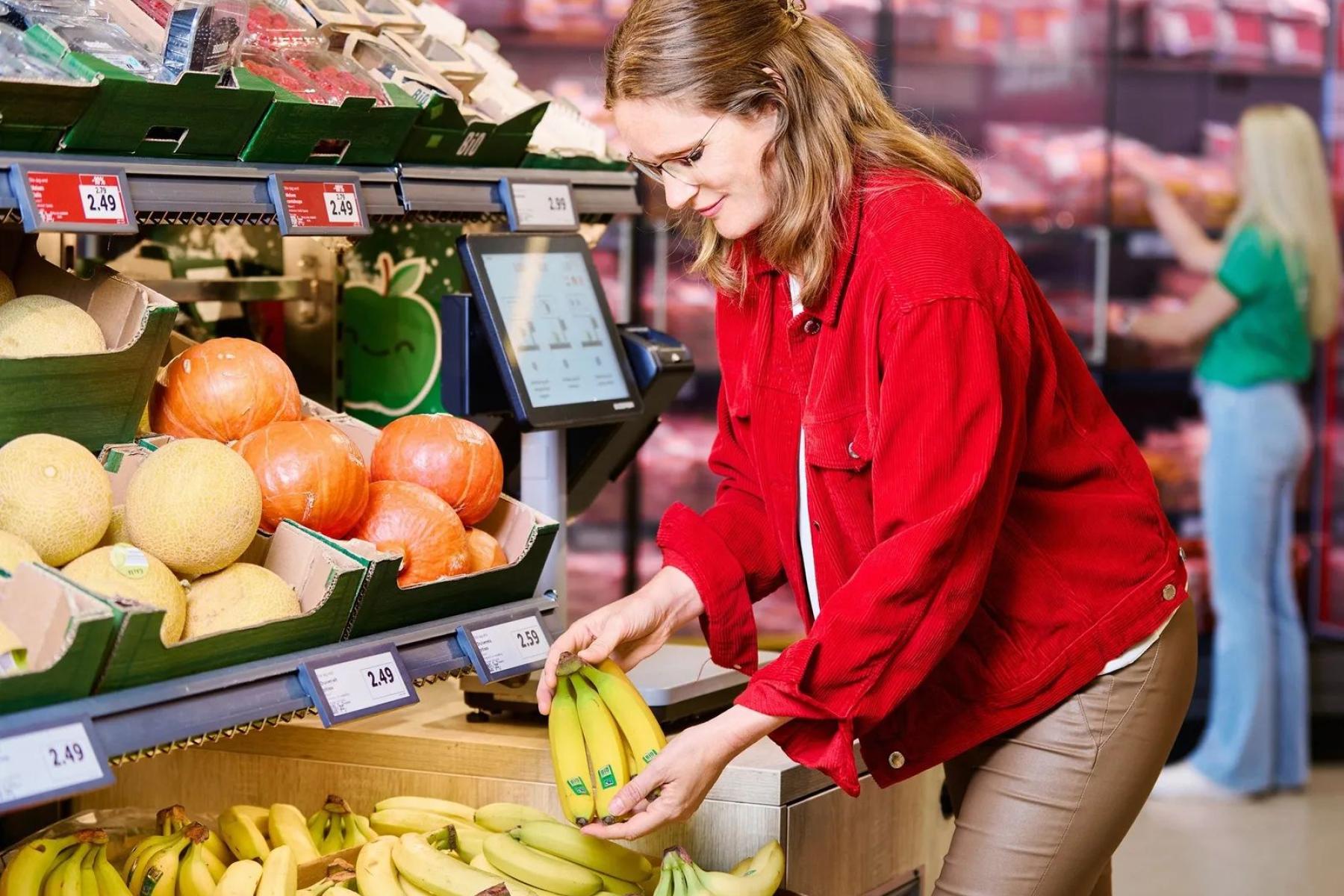 Frau steht vor Obstregal und hält Bananen in der Hand