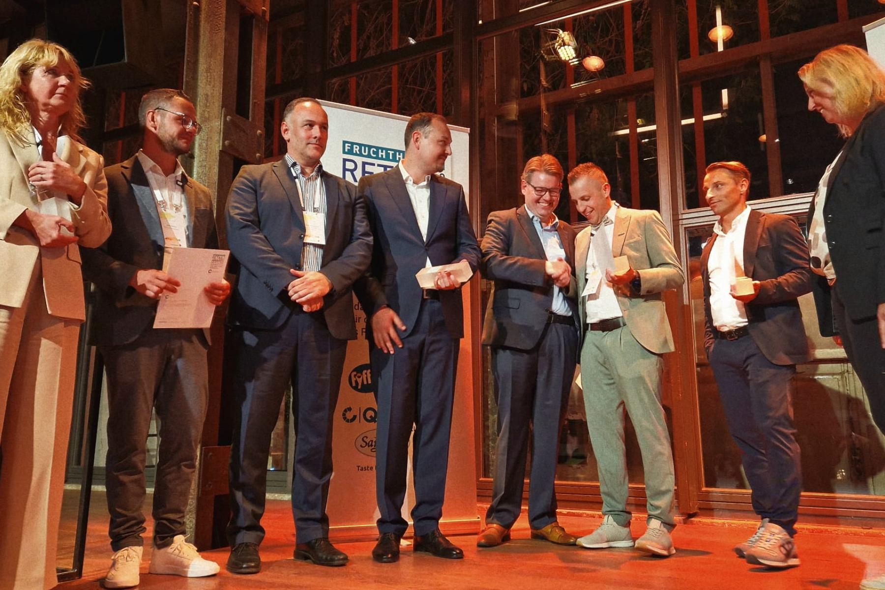 Männer und Frauen stehen mit Trophäe in der Hand auf der Bühne