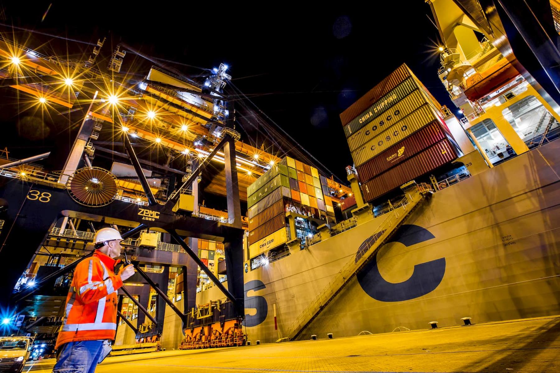 Mitarbeiter im Hafen Rotterdam vor einem Containerschiff beim nächtlichen Umschlag von Containern.