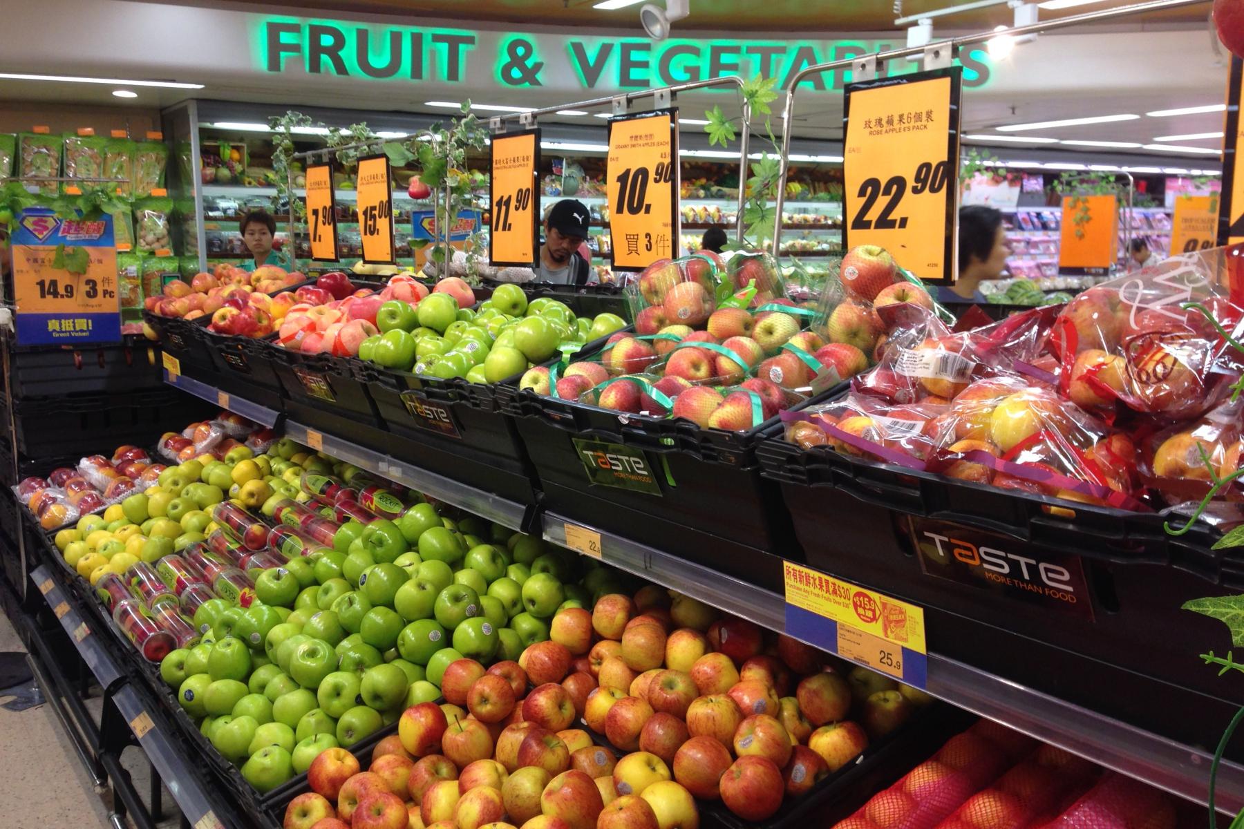 Obstauslage in einem Supermarkt in Hongkong mit roten und grünen Äpfeln, lose und verpackt, sowie darüber angebrachten Preisschildern.