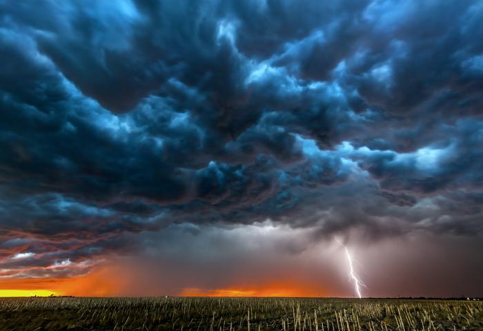 Gewitterwolken über einem Feld bei Sonnenuntergang mit einem Blitzschlag am Horizont