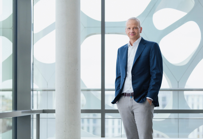 Markus Kamieth, Vorstandsvorsitzender von BASF, steht in einem modernen Gebäude mit großen Fenstern, trägt einen dunkelblauen Blazer, weißes Hemd und graue Hose