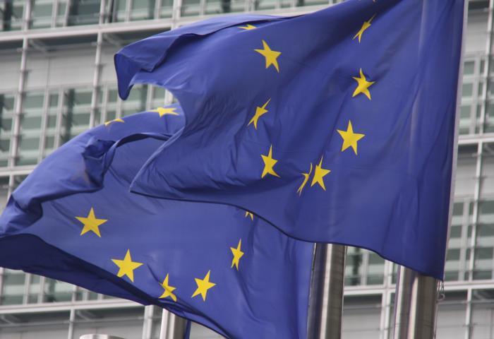 Zwei EU-Fahnen (je zwölf gelbe Sterne auf blauem Hintergrund) wehen vor einem modernen Gebäude