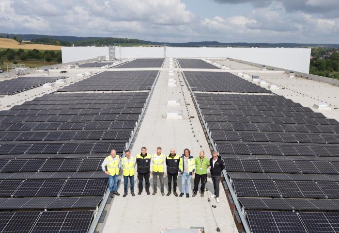 Acht Personen in Sicherheitswesten stehen auf einem Flachdach zwischen großen Solarpanelreihen unter bewölktem Himmel