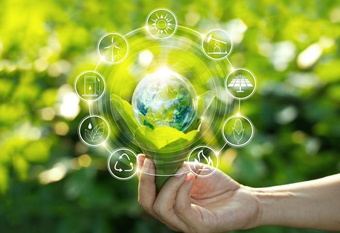 Hand hält eine kleine Pflanze mit Erde, darüber schwebt eine Erde und rundherum Symbole für erneuerbare Energien und Umweltschutz