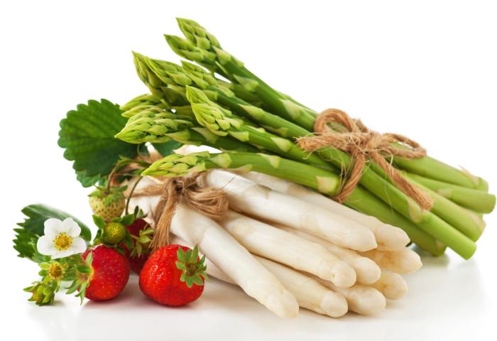 ündel grüner und weißer Spargel zusammengebunden mit Juteband, daneben frische Erdbeeren und Erdbeerblüten