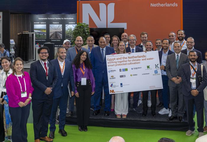 Gruppe von Personen auf einer Messe vor einem orangefarbenen Stand mit dem Schriftzug 'Netherlands', halten ein großes Schild mit dem Titel 'Egypt and the Netherlands: working together for climate- and water-smart protected cultivation'