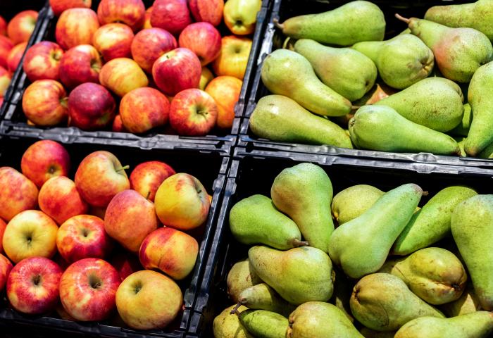 Rote und gelbe Äpfel sowie grüne Birnen liegen in schwarzen Kisten in der Auslage