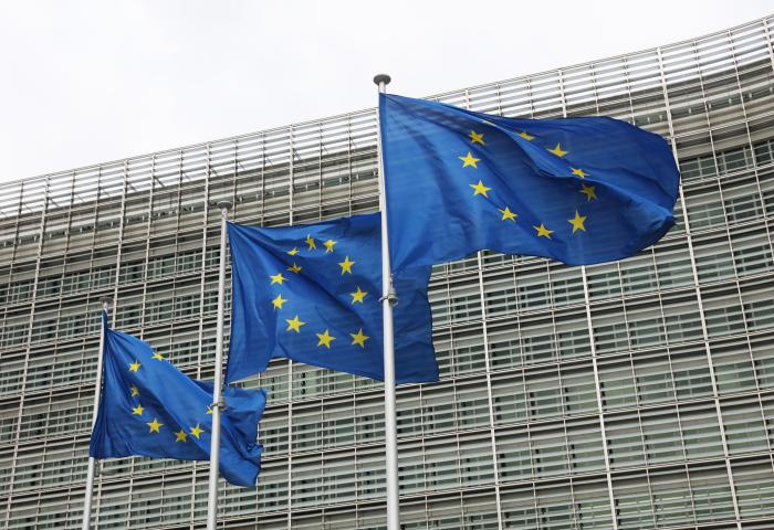 Drei wehende Europaflaggen vor einem modernen Glasgebäude