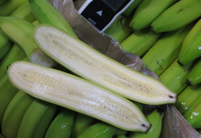 der Länge nach aufgeschnittene grüne Banane und ganze Bananen in Karton