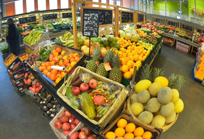 Obst- und Gemüseabteilung in einem Supermarkt mit verschiedenen Früchten wie Bananen, Ananas, Orangen, Melonen und Äpfeln auf Verkaufstischen