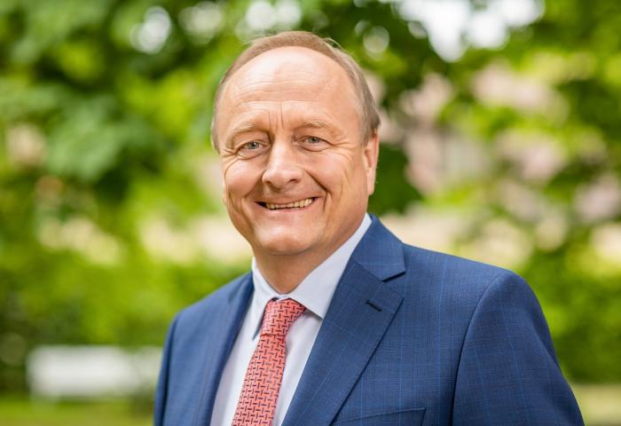 Joachim Rukwied trägt einen blauen Anzug und eine rote Krawatte, steht vor unscharfem grünem Hintergrund