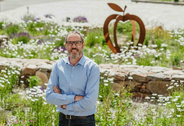 Gerhard Eberhöfer stehend mit verschränkten Armen, im Hintergrund Gräser und Wildblumen