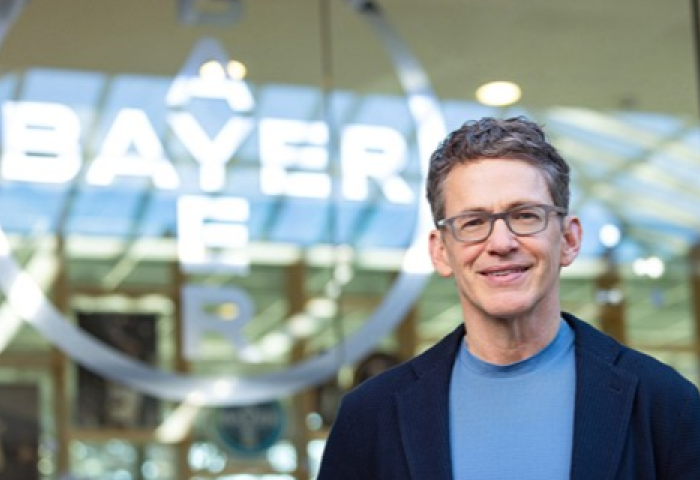 Bill Anderson steht vor dem Bayer-Logo in einem modernen Gebäude