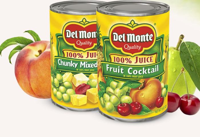 Zwei Del Monte Dosen mit Fruchtcocktail und Chunky Mixed Frucht in 100% Fruchtsaft, umgeben von Pfirsich, Trauben und Kirschen