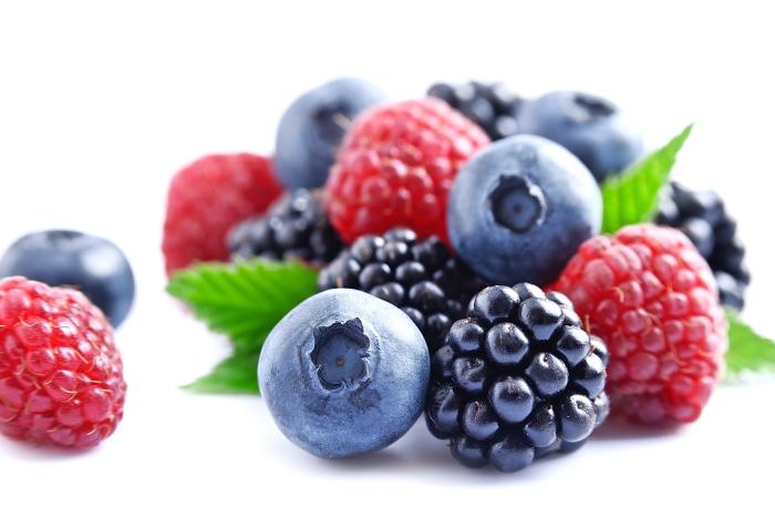 Verschiedene Beeren wie Himbeeren, Heidelbeeren und Brombeeren mit grünen Blättern auf weißem Hintergrund