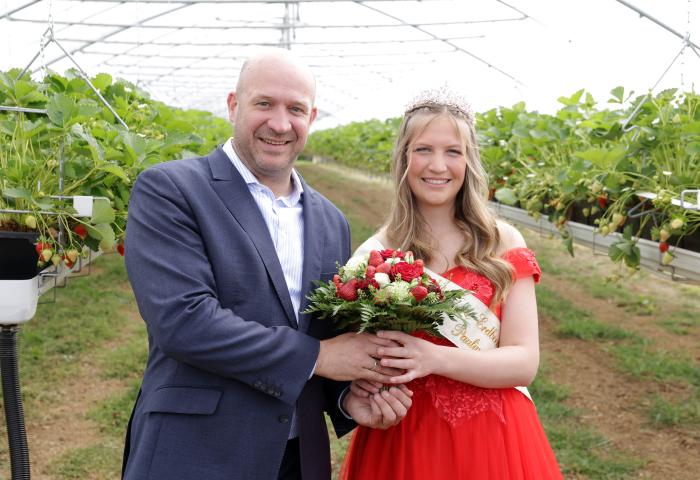 Landwirtschaftsminister Ingmar Jung und Erdbeerkönigin Paulina I. mit Krone und Schärpe, die einen Erdbeerstrauß hält, in einem Gewächshaus