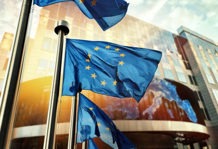 Mehrere wehende Europaflaggen vor einem modernen Gebäude mit Glasfassade