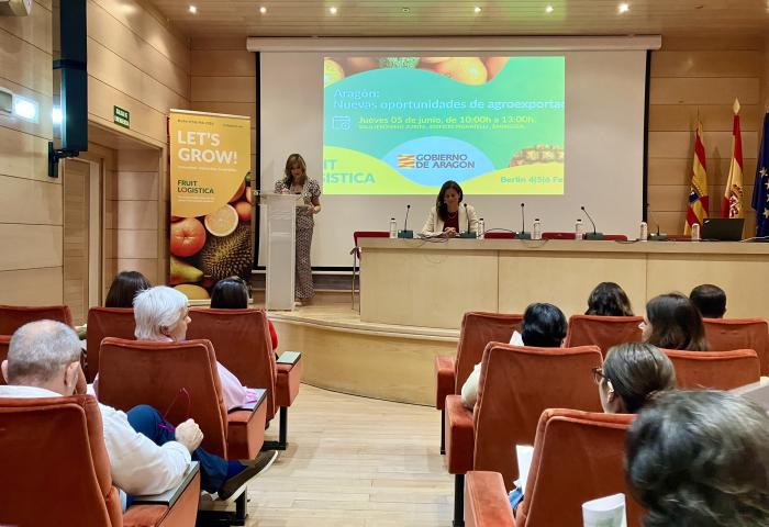 Amparo Cuéllar Hernandis spricht am Rednerpult, Silvia de Juanes sitzt am Tisch, Veranstaltung zur Förderung von Agrarexporten in Aragonien, Publikum im Saal