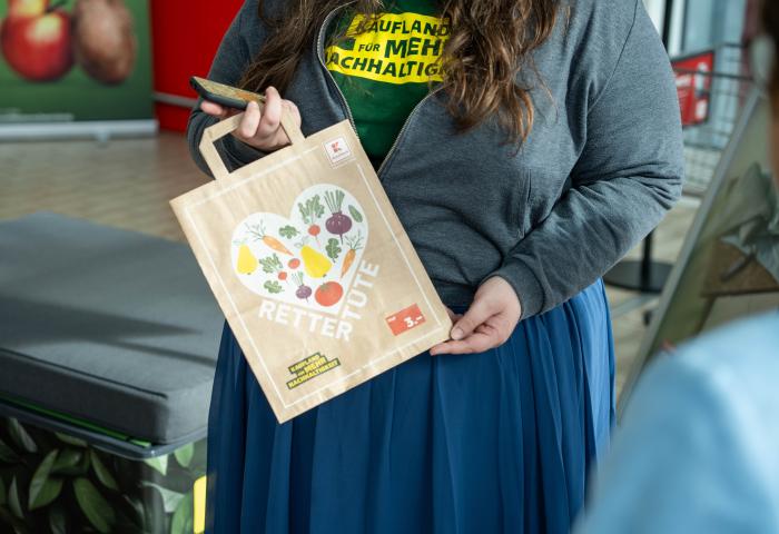 Frau hält eine Papiertüte mit Herzmotiv und der Aufschrift 'Rettertüte' und '3 €' in der Hand