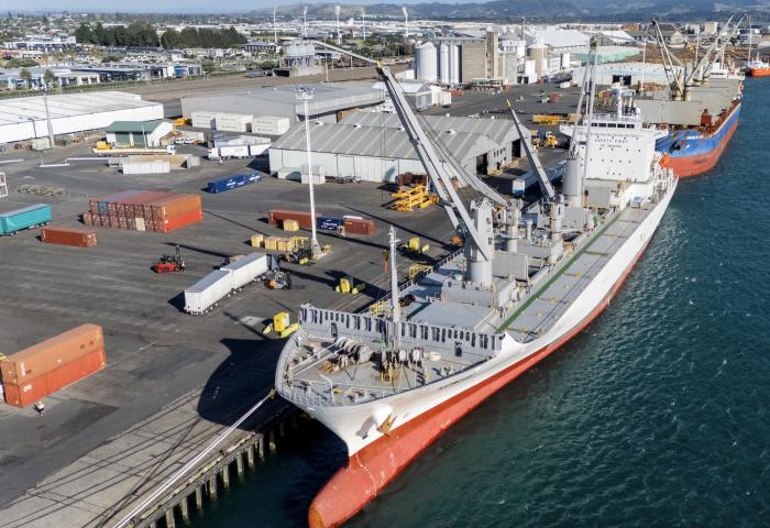Großes Frachtschiff am Hafen von Tauranga, beladen mit Containern und Kiwifrüchten, Hafenanlagen und Wasser sichtbar