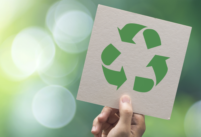 Hand hält Karte mit grünem Recycling-Symbol vor unscharf grünem Hintergrund