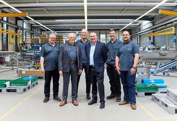 Johannes Günther, Rudolf Hans Zillgith, Stephan Zillgith, Eric Lefebvre stehen in einer Fabrikhalle mit Maschinen und Förderbändern