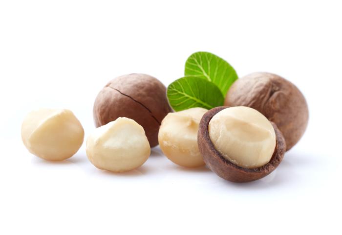 Macadamianüsse, einige geschält und einige in Schale, mit grünen Blättern auf weißem Hintergrund