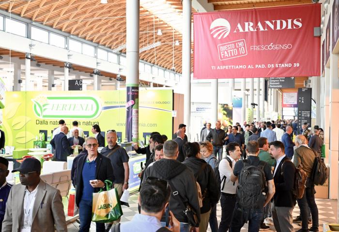 Messehalle mit zahlreichen Besuchern, Ständen von Unternehmen wie Arandis und Ferteva, Informationsbanner und helle, offene Architektur mit Holzdach.