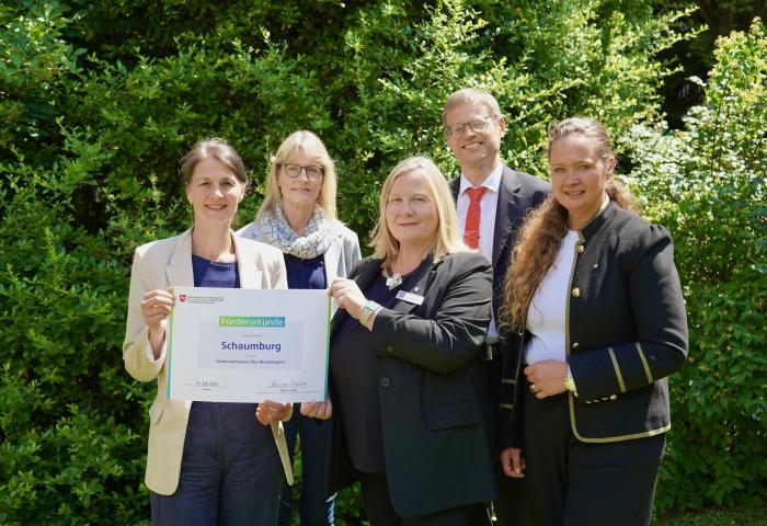 Fünf Personen stehen vor grünem Gebüsch, eine hält eine Förderurkunde mit der Aufschrift 'Schaumburg' für die Öko-Modellregion Schaumburg