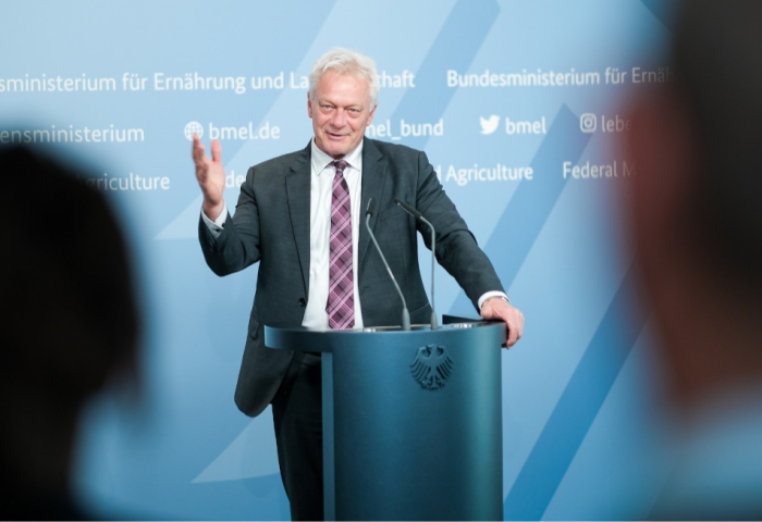 Alois Rainer steht hinter einem Rednerpult mit Bundesadler, gestikuliert mit der rechten Hand