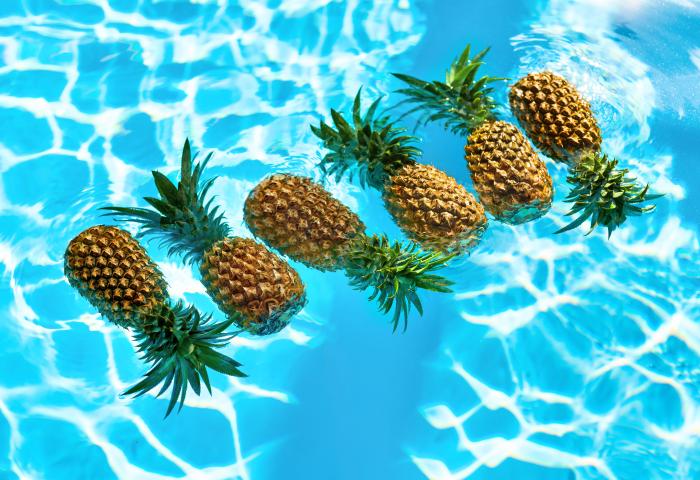 Sechs Ananas schwimmen auf der Wasseroberfläche eines Pools mit blau reflektierendem Wasser