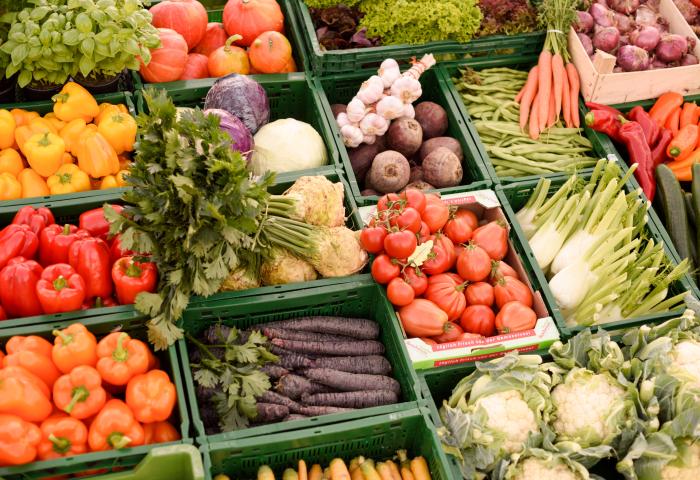 Marktstand mit verschiedenen frischen Gemüsesorten wie Paprika, Karotten, Tomaten, Blumenkohl, Knoblauch und Salat in grünen Kisten