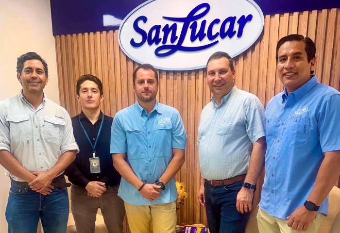 Vertreter von SanLucar und Sun World stehen vor einem SanLucar-Logo an einer Holzpaneelwand