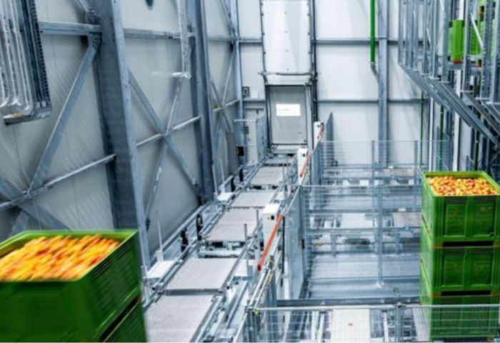 Innenansicht des Smart Fruit Hub mit automatisierten Förderbändern und grünen, vollen Kisten in einem Lagerhaus mit Metallstruktur