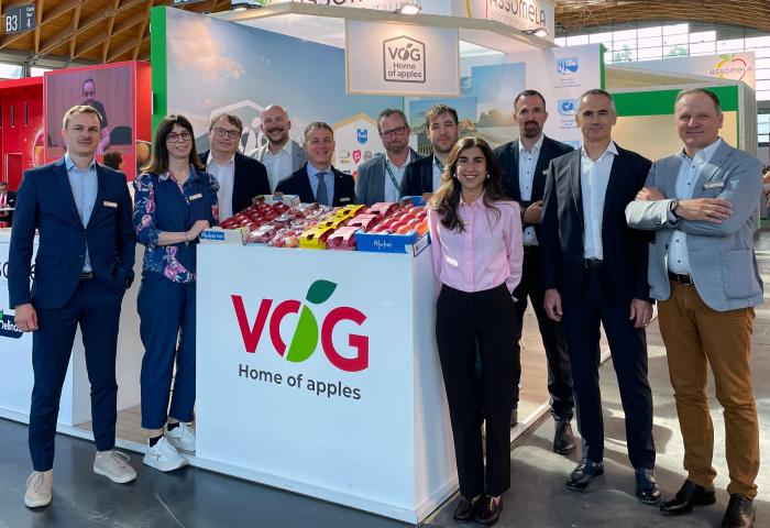 Das Team VOG steht hinter einem Messestand mit dem Logo 'VOG Home of apples' der mit verschiedenen Apfelsorten in Kisten dekoriert ist