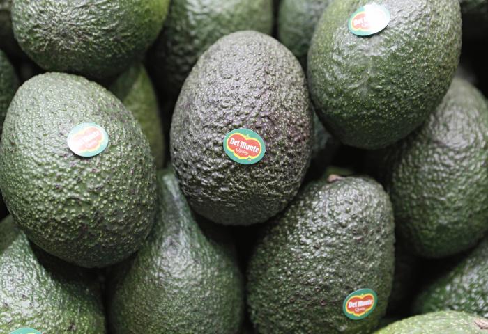 Mehrere grüne Avocados mit Del Monte Aufklebern, eng aneinander liegend