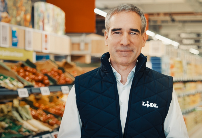 Friedrich Fuchs, Lidl-Deutschlandchef steht in einem Supermarkt mit Obst- und Gemüseregalen im Hintergrund.