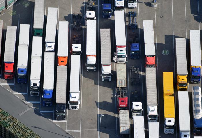 Luftaufnahme eines Parkplatzes mit mehreren Lkw in Reihen. Die Lkw haben unterschiedliche Farben, darunter rot, blau, gelb und weiß.