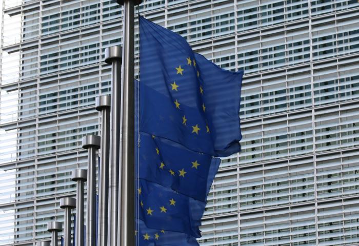 Mehrere, in einer Reihe stehende EU-Flaggen am Mast vor einem modernen Gebäude