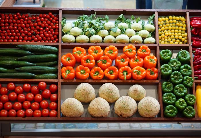 Eine Gemüseauslage mit verschiedenen Sorten. Darunter rote und gelbe Kirschtomaten, orangene und grüne Paprika sowie Salatgurken